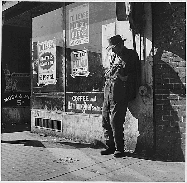Great Depression: unemployed, destitute man leaning against vacant store, San Francisco (1935). By Dorothea Lange. Via Wikimedia Commons.